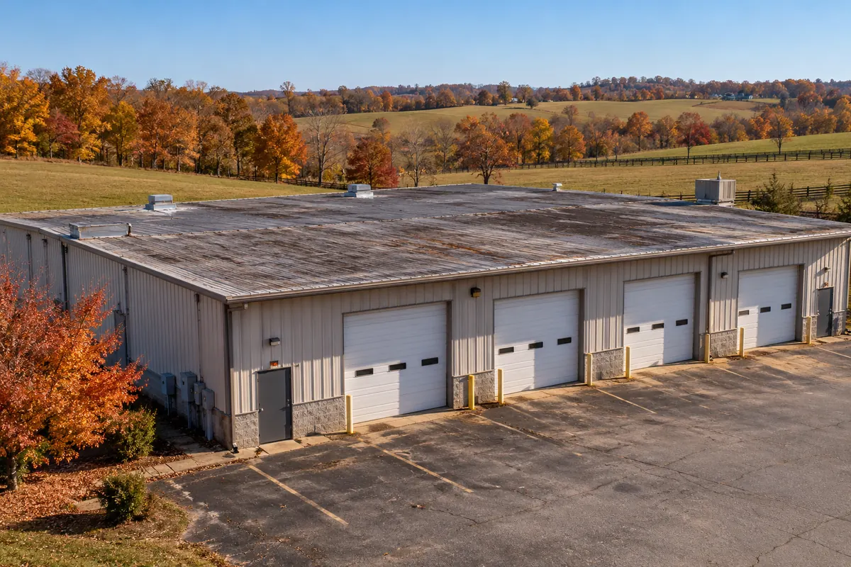 Metal warehouse with four loading doors and a worn roof on a rural Kentucky lot